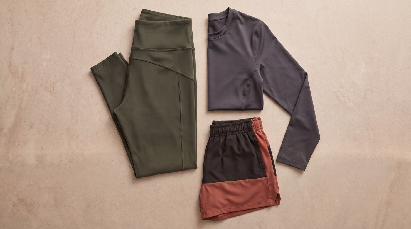 Olive leggings, a charcoal long-sleeve performance top, and color-blocked training shorts laid flat