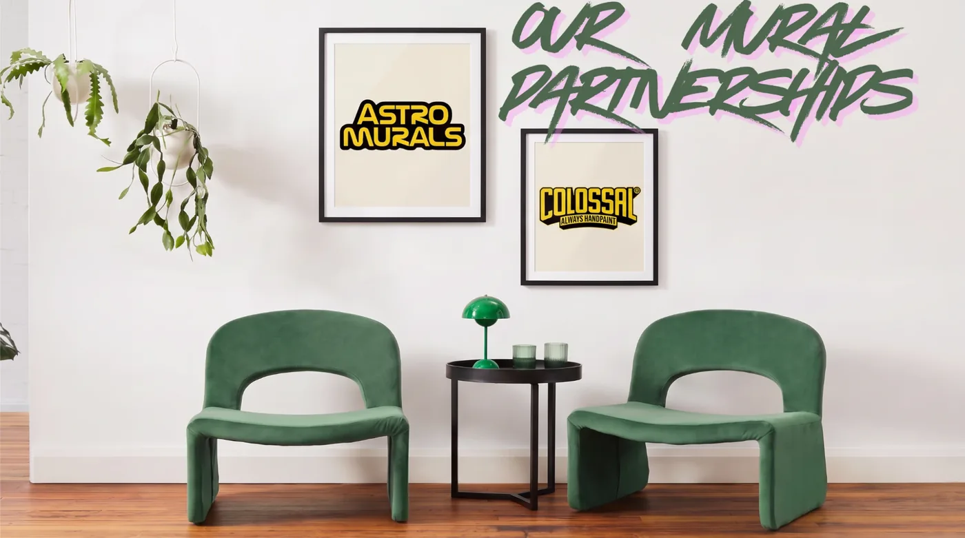Framed Astro Murals and Colossal logos on a white wall above two green chairs, under the painted words Our Mural Partnerships